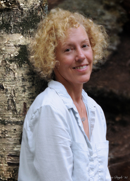 Author, Susanne Davis. This photo shows her with blond curls around a smiling face as she turns to face the camera. She is wearing a soft pale blue button up blouse.